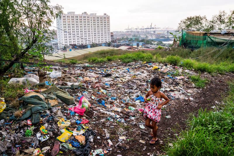 FILE PHOTO: A girl walks past plastic waste dumped at a former landfill in Manila