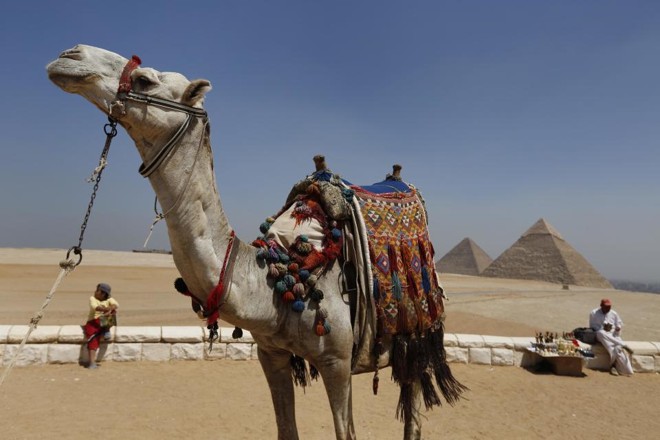In this Saturday, Sept. 7, 2013 photo, a tourist guide sits close to his camel as a vendor waits for tourists to offer souvenirs for sale at the historical site of the Giza Pyramids, near Cairo, Egypt. Before the 2011 revolution that started Egypt's political roller coaster, sites like the pyramids were often overcrowded with visitors and vendors, but after a summer of coup, protests and massacres, most tourist attractions are virtually deserted to the point of being serene. (AP Photo/Lefteris Pitarakis)