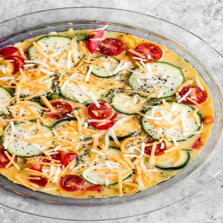 Uncooked eggs with zucchini, tomatoes, and cheese in a bowl