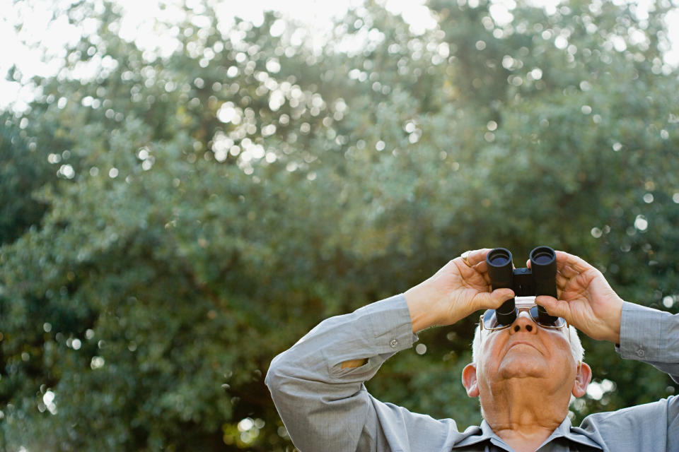 A senior man looks up at the sky through binoculars.