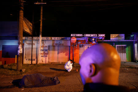 A forensic worker takes photos next to the body of a man who was thrown from a car into the street after he was killed, in Tegucigalpa, Honduras, August 6, 2018. REUTERS/Edgard Garrido