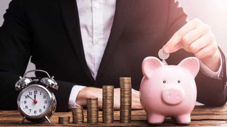 Businessperson's Hand Putting Coin In Piggybank