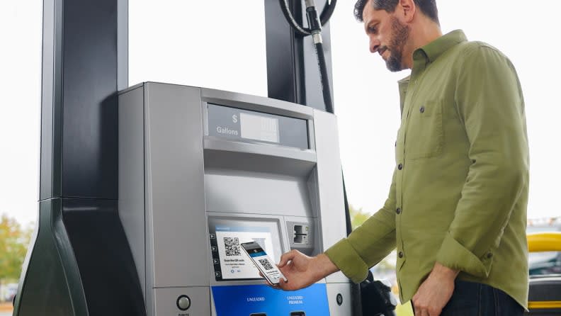 A person shown standing by a gas pump paying for gas with their smart phone.