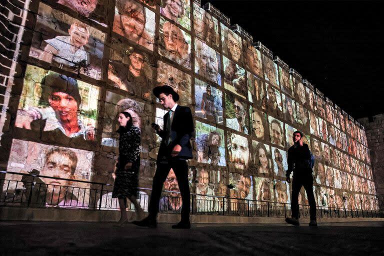 La gente camina fuera de los muros de la ciudad vieja de Jerusalén, en la que se proyectan imágenes de los rehenes secuestrados por militantes palestinos en el ataque del 7 de octubre y actualmente retenidos en la Franja de Gaza, el 6 de noviembre de 2023, en medio de las batallas en curso entre Israel y el grupo militante Hamas.