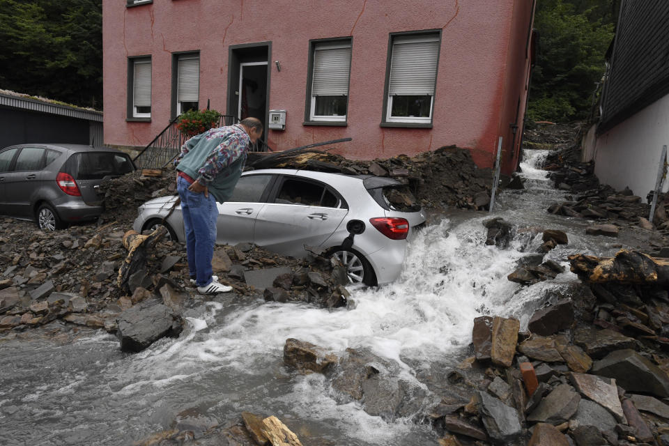 A man looks at a car that is covered in Hagen, Germany, Wednesday, July 15, 2021 with the debris brought by the flooding of the 'Nahma' river the night before. The heavy rainfalls had turned the small river into a raging torrent. (Roberto Pfeil/dpa via AP)