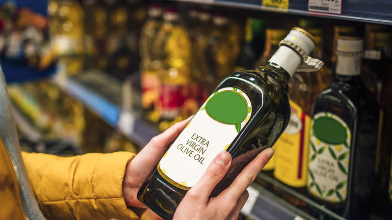 hands holding bottle of extra virgin olive oil in grocery store