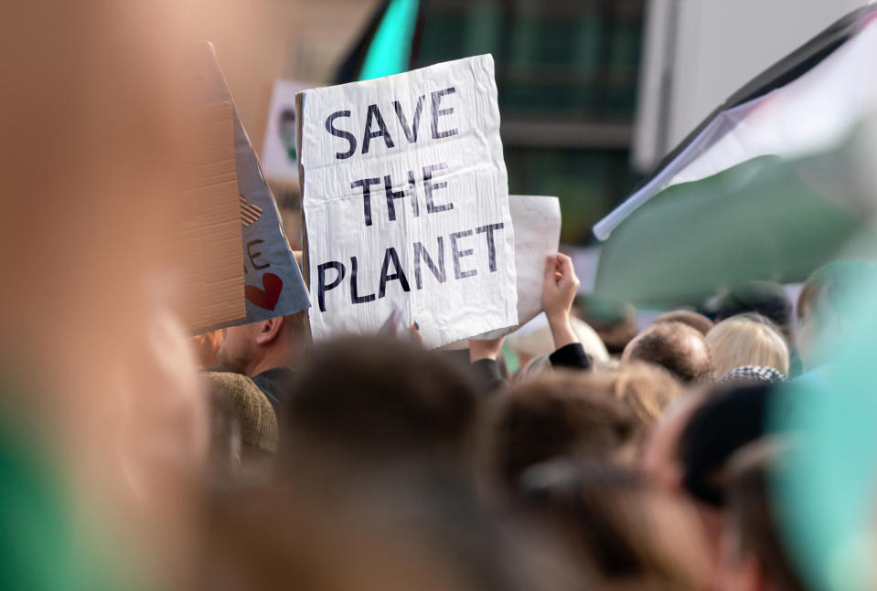 People holding signs at a protest, one prominently reads "Save the Planet."