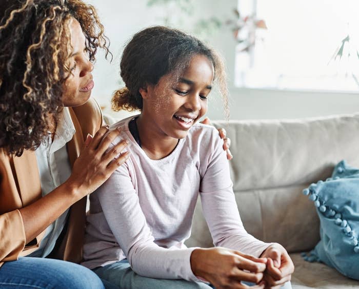 Unknown woman comforting a young girl on a couch. The woman has her hand on the girl's shoulder as they both smile