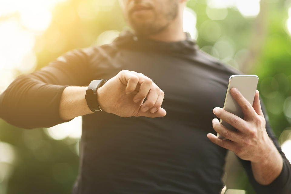 Closeup of unrecognizable man checking workout data on fitness tracker after intensive training outdoors, free space