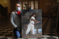 In this Wednesday, April 29, 2020, photo, baseball artist Graig Kreindler poses for a photograph in the lobby of his Brooklyn residence in New York with an unfinished painting of Hall of Famer Josh Gibson showing off his swing. The painting is based on a 1939-40 photograph from Gibson's days with the Cangrejeros (Crabbers) de Santurce, part of the Puerto Rico semi-professional league. That photograph was later used for for Gibson's 1950-51 Toleteros baseball card, now a pricey collectible. During the first half of the 20th century, many African-American players participated in winter ball games in Latin America, earning extra money and escaping racism in the United States. Some 230 of Kreindler's paintings are part of an exhibit celebrating the centennial fo the Negro National League at the National Negro Leagues Baseball Museum in Kansas City, Mo. The museum was forced to temporarily shut down due to concerns over the coronavirus outbreak, but is aiming to reopen in June. (AP Photo/Kathy Willens)