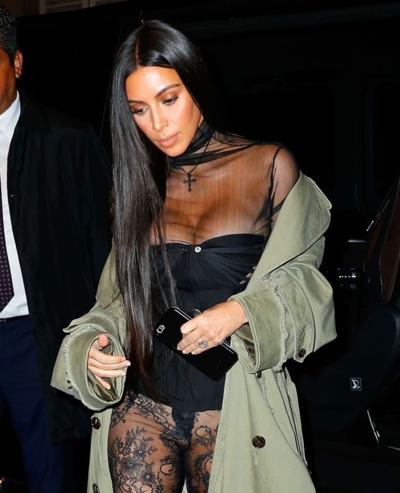 Kim Kardashian West vêtue d'une tenue transparente en dentelle, d'un manteau vert et d'un ras de cou orné d'une croix