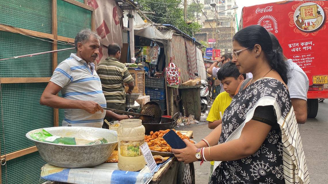 A woman in Kolkata pays roadside pakoda (fritter) seller Sailender Kumar by scanning a QR code from her mobile phone UPI app.