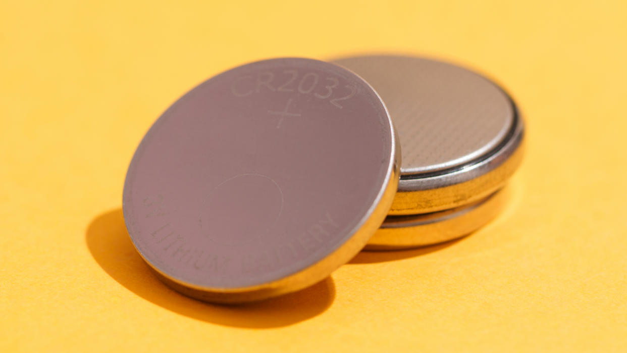  High angle view of three used CR2032 lithium button cell batteries isolated on yellow background. 