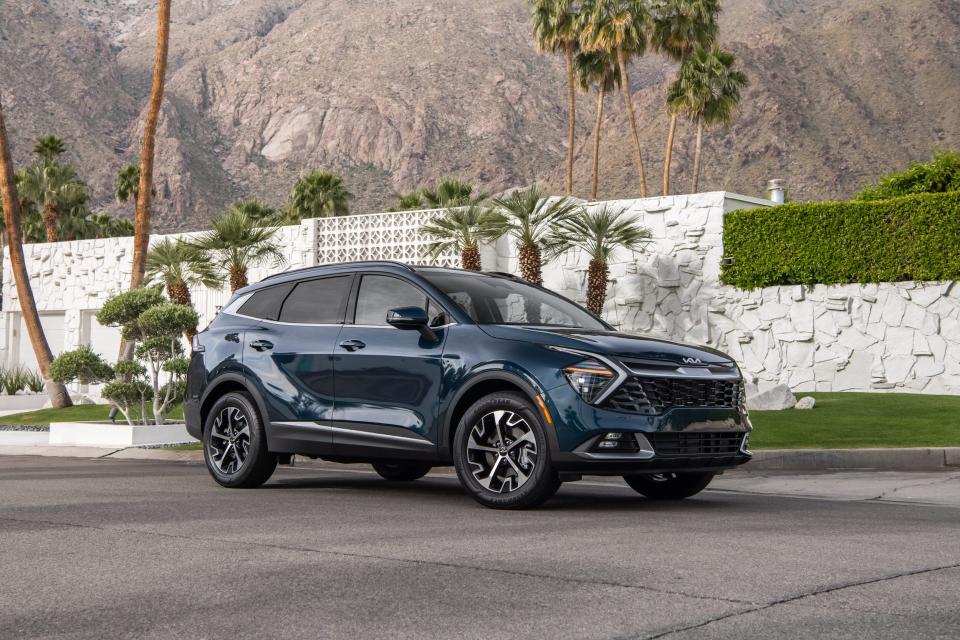 The 2023 Kia Sportage Hybrid is parked outside a white retaining wall and a mountain in the distance.