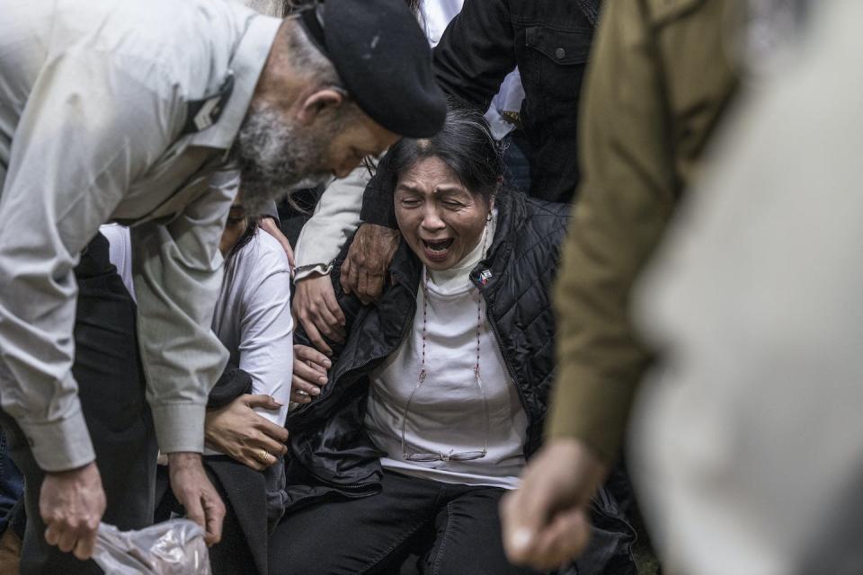 A woman screams and cries as she kneels down and people reach out to touch her. She appears to be looking toward the ground.