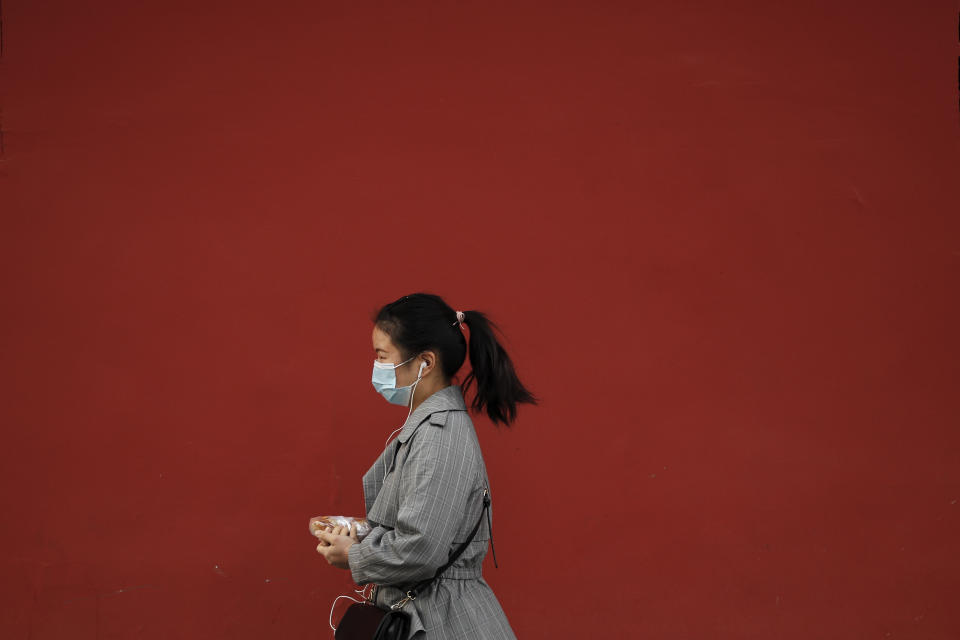 A woman wearing a face mask to help curb the spread of the coronavirus holds her breakfast meal while walking by a red wall in Beijing, Wednesday, Oct. 14, 2020. (AP Photo/Andy Wong)