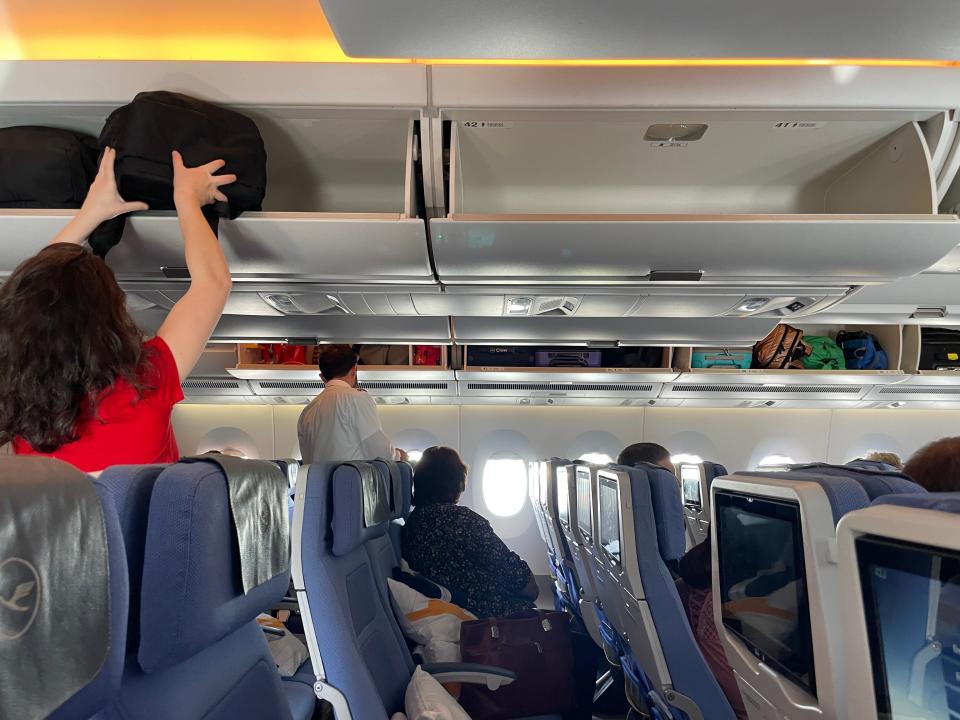 A passenger in the back of the plane put her bag in the overhead bin.