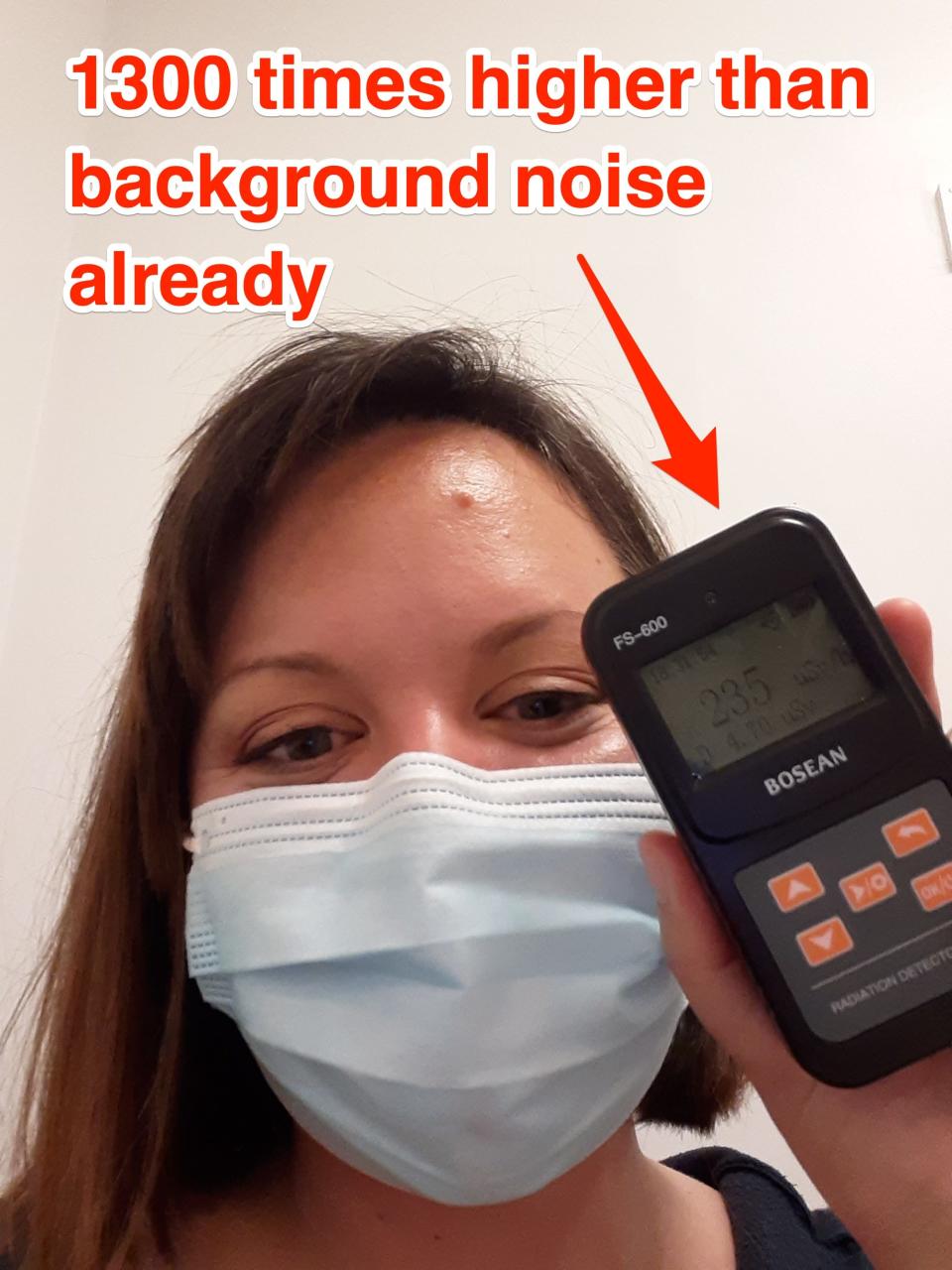 Marianne Guenot is wearing a mask and holding up a Geiger counter. An arrow poitns to the counter, text reads "1300 times higher than background noise already"