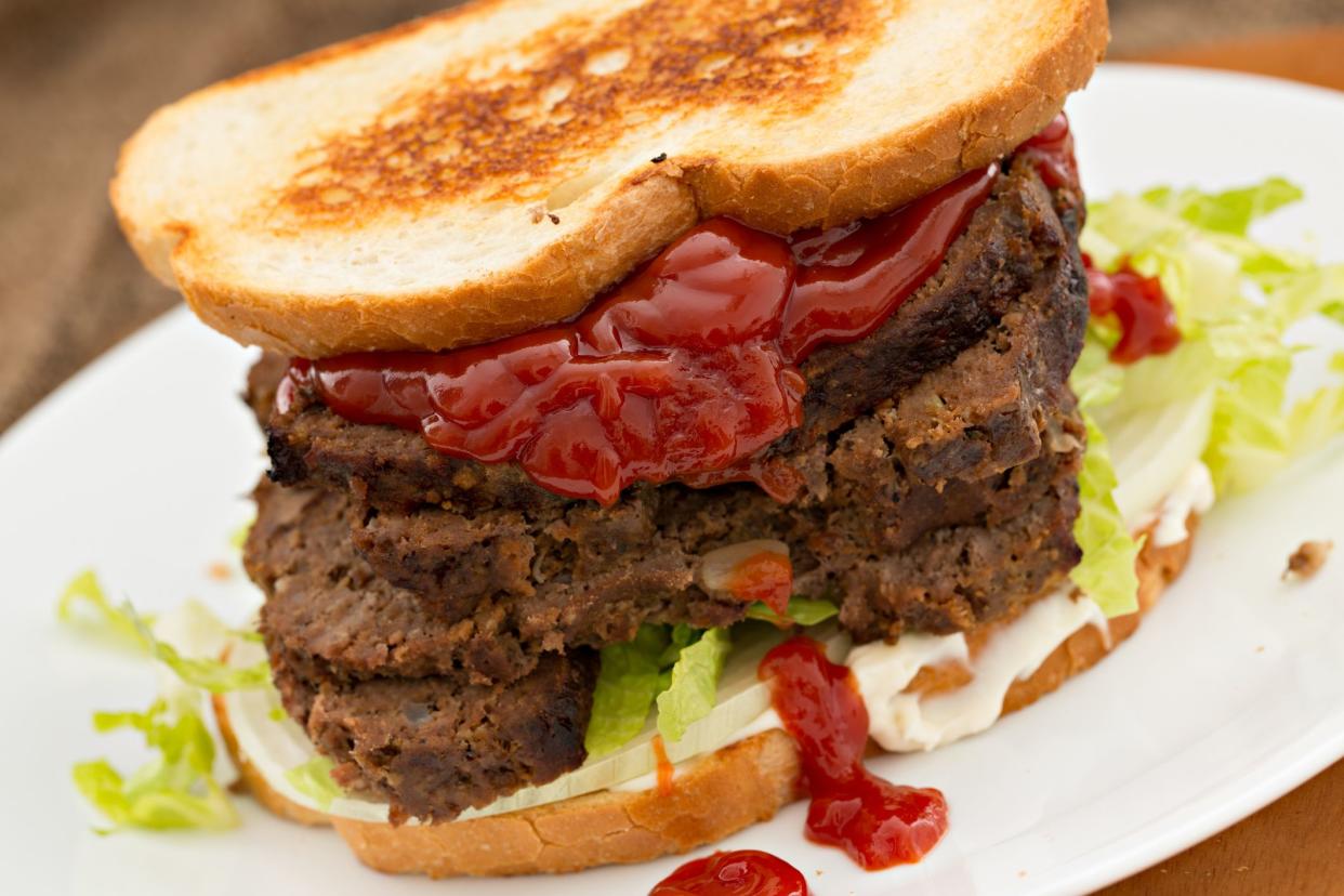 A high angle close up shot of a large meatloaf sandwich heavy on the ketchup.