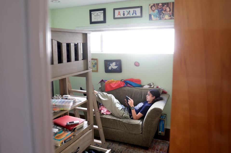 A teenager looks at a cellphone while lying on a couch