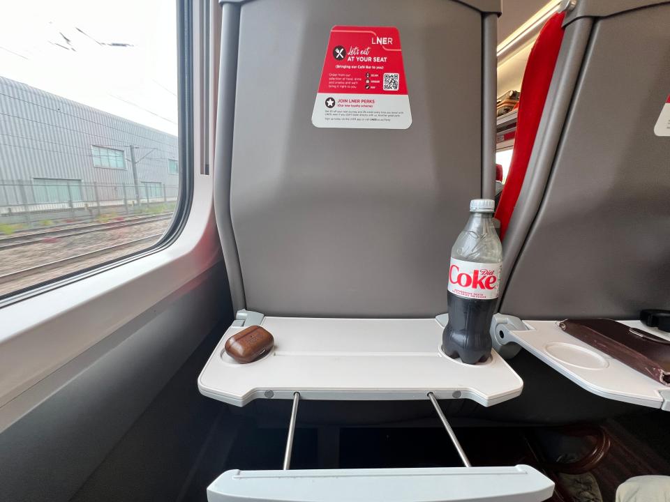 A seatback and tray table with headphones and Diet Coke on top, on an LNER Azuma train.