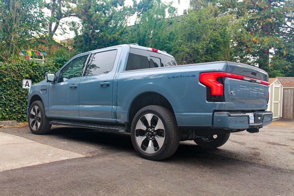 A blue 2023 Ford F-150 Lightning Platinum parked in a parking lot, with trees in the background.