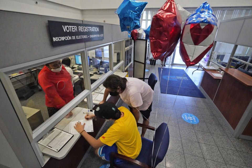 Lucas Saez, foreground, 22, fills out his voter registration form as his father Ramiro Saez, center rear, looks on, Tuesday, Oct. 6, 2020, at the Miami-Dade County Elections Department in Doral, Fla. Florida Gov. Ron DeSantis extended the state's voter registration deadline after heavy traffic crashed the state's online system and potentially prevented thousands of enrolling to cast ballots in next month's presidential election. Saez attempted to register to vote six times the night before without any luck. (AP Photo/Wilfredo Lee)