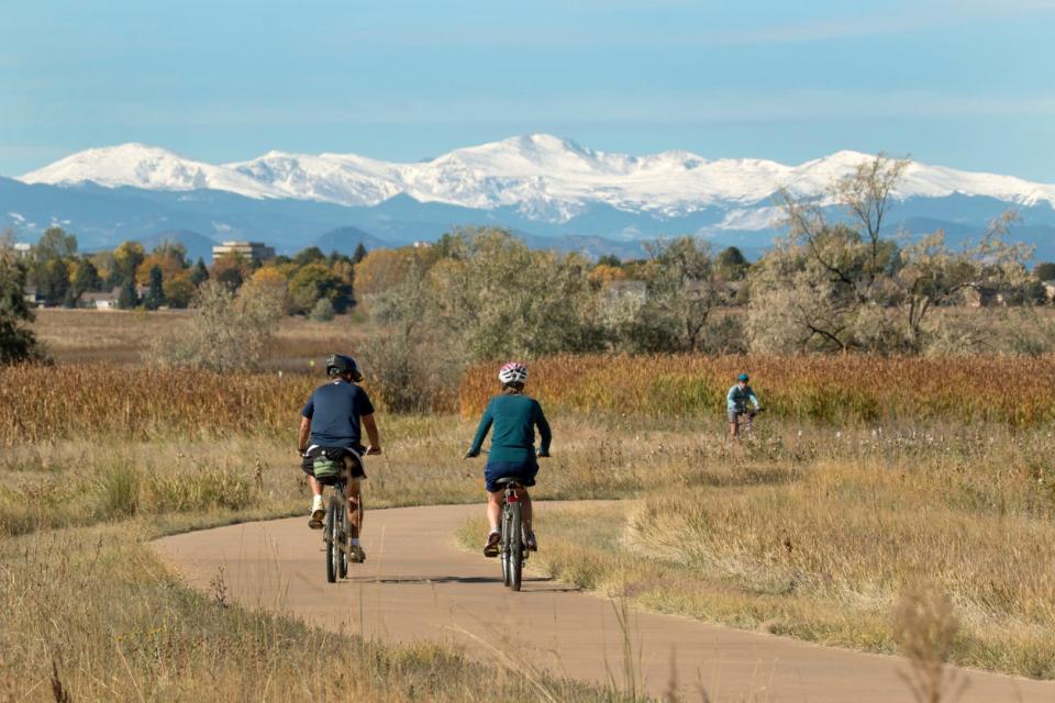 Riding the paved path around the lake with a snowy Mount Evans in the background, visitors enjoy riding their bicycles in Colorado's Cheery Creek State Park in Denver. 