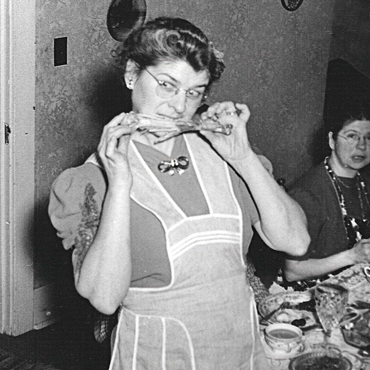 1930s woman jokingly biting a turkey leg while family looks on in confusion 