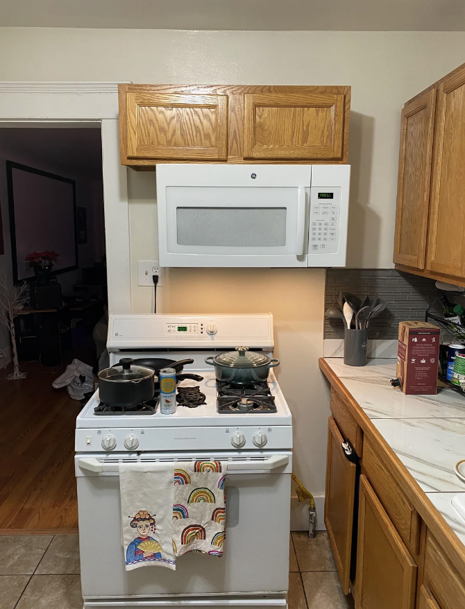 A kitchen with a microwave on the stove, a pot on the stove, and a towel hanging on the oven door