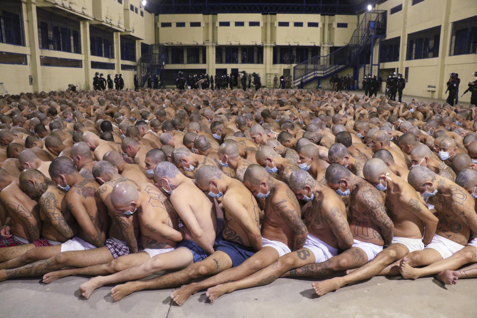In this photo released by the El Salvador Presidency Press Office, inmates are lined up during a security operation under the watch of police at the Izalco prison in San Salvador, El Salvador, Saturday, April 25, 2020. Authorities crammed the prisoners, albeit wearing masks, tightly together in prison yards while searching their cells. President Nayib Bukele ordered the crackdown after more than 20 people were murdered in the country Friday and intelligence suggested the orders came from imprisoned gang leaders. (El Salvador President Press Office via AP)