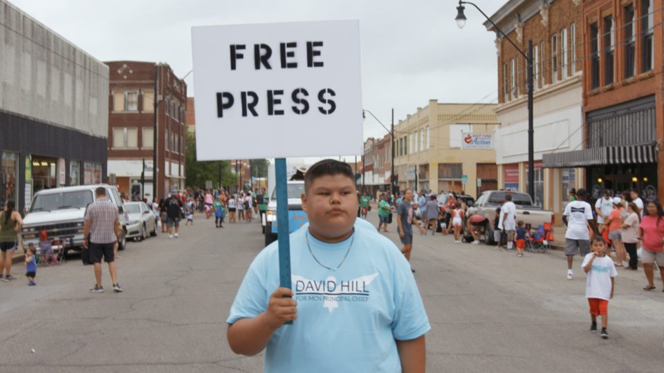 A boy holds a sign saying "Free Press" in 'Bad Press'
