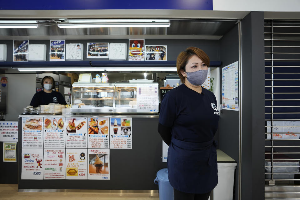 Fast-food restaurant owner Atsuko Yamamoto responds to an interview with The Associated Press in front of her shop, Penguin, in Futaba Business Incubation and Community Center in Futaba town, northeastern Japan, Wednesday, March 2, 2022. Her daughter Mika, background, helps her mother cook at the restaurant. Yamamoto restarted Penguin, one of her family's old businesses, in 2020, when the community center opened for the public, as she wanted to help bring local people back together, as part of her way of the area reconstruction, following the 2011 earthquake. (AP Photo/Hiro Komae)