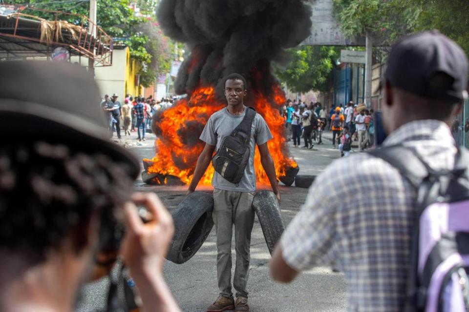 A protester, holding tires, poses for a photo in front of a burning barricade during a protest against rising insecurity in Port-au-Prince, Haiti, Thursday, Dec. 10, 2020. Port-au-Prince has seen an increase in gang violence and kidnappings.
