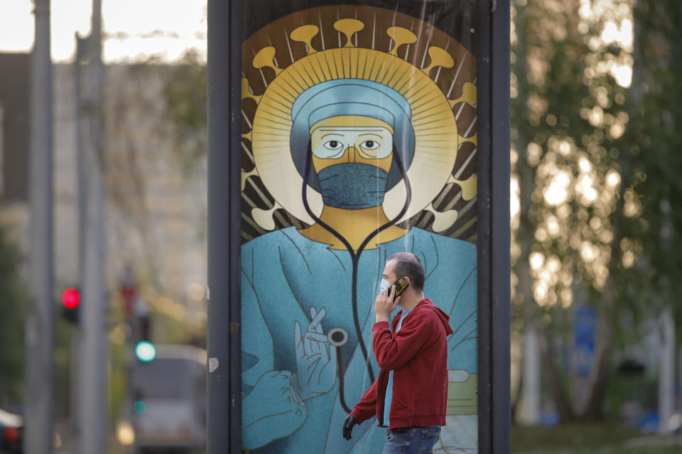 A man walks by a depiction of a medical staff wearing protective equipment, executed in the style of Christ Pantocrator, in Bucharest, Romania, Wednesday, April 29, 2020. The artwork, among others depicting medical staff in the manner of religious icons, created by designer Wanda Hutira, is part of a campaign called Thank You Doctors, meant to raise awareness to the work of medical staff fighting the COVID-19 pandemic. Following public pressure by Romania's influential Orthodox church the artworks, described as "blasphemous", will be removed from all locations in the Romanian capital, according to the agency behind the project.(AP Photo/Vadim Ghirda)