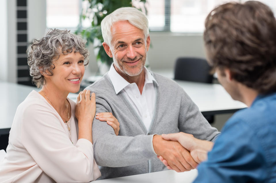 An older couple shakes hands with a younger banker at a desk.