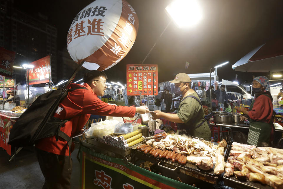 Hong Tsun-ming, left, a Taiwanese of Hong Kong descent, distributes election flyers to a vendor at a night market in Taichung city, Central Taiwan, on Nov. 30, 2023. As Taiwan’s presidential election approaches, many immigrants from Hong Kong, witnesses to the alarming erosion of civil liberties at home, are supporting the ruling Democratic Progressive Party. (AP Photo/Chiang Ying-ying)