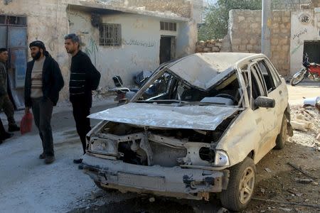 Residents stand near a damaged car in the town of Darat Izza, province of Aleppo, Syria February 28, 2016. REUTERS/Ammar Abdullah