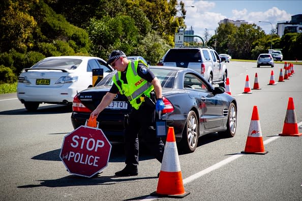 A Queensland police officer moves a stop sign at a vehicle checkpoint on the Pacific Highway on the Queensland - New South Wales border.