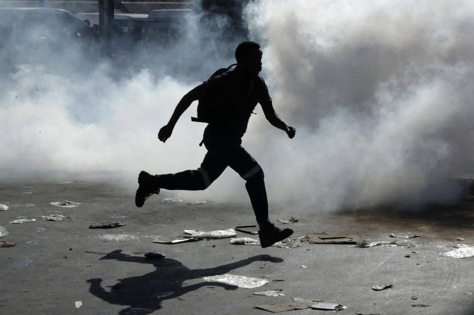 A man runs away from teargas after making off with goods from a store in Germiston, east of Johannesburg, South Africa, Tuesday, Sept. 3, 2019. Police had earlier fired rubber bullets as they struggled to stop looters who targeted businesses as unrest broke out in several spots in and around the city. (AP Photo/Themba Hadebe)