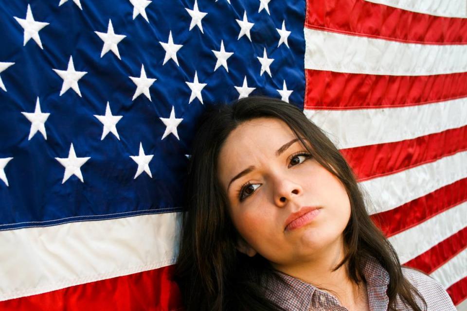 Representación artística de una mujer latina desilucionada recostada sobre una bandera de Estados Unidos.