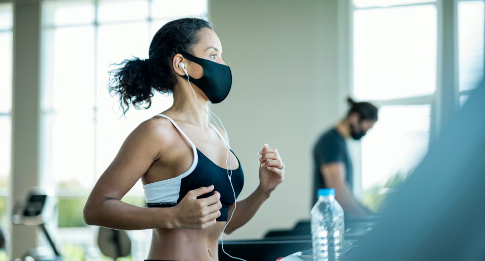 woman wearing sports bra running on a treadmill wearing a black face mask and headphones