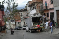 Residents help to unload bags of basic food staples, such as pasta, sugar, flour and kitchen oil, provided by a government food assistance program, as a couple on a motorcycle drive past in front of they in the Santa Rosalia neighborhood of Caracas, Venezuela, Saturday, April 10, 2021. The program known as Local Committees of Supply and Production, CLAP, provides subsidized food for vulnerable families, especially now in the midst of a quarantine to stop the COVID-19 pandemic that has left many without income. (AP Photo/Matias Delacroix)