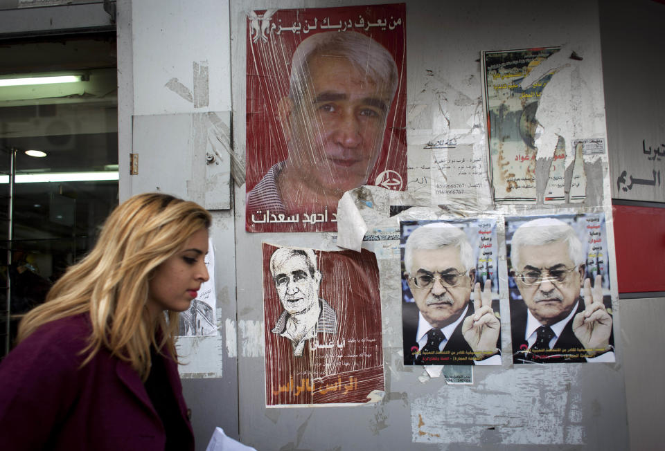 A Palestinian woman walks past posters with pictures of Palestinian President Mahmoud Abbas, two at right, and Ahmed Saadat, leader of the Popular Front for the Liberation of Palestine who is currently imprisoned by Israeli, in the West Bank city of Ramallah, Wednesday, March 19, 2014. The Palestinians threatened Wednesday to resume their campaign for international recognition at the United Nations if Israel calls off a planned release of Palestinian prisoners, deepening a crisis that has threatened to derail U.S.-led Mideast peace efforts. (AP Photo/Nasser Nasser)