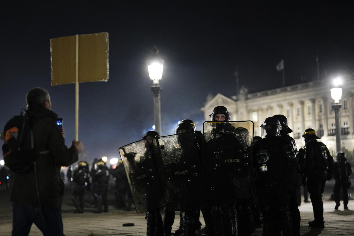 A protester faces police officers at Concorde square after a demonstration, in Paris, Thursday, March 16, 2023. French President Emmanuel Macron has shunned parliament and imposed a highly unpopular change to the nation's pension system, raising the retirement age from 62 to 64. (AP Photo/Lewis Joly)