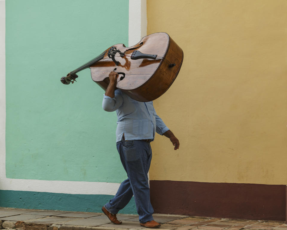 Person carrying a large double bass on their shoulder walking by a building