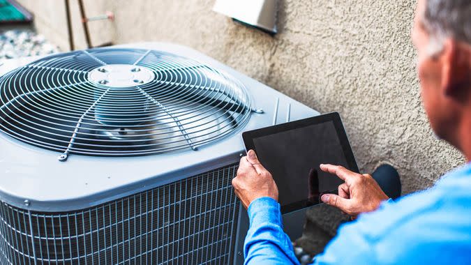 Maintenance engineer using digital tablet to inspect air conditioning unit.