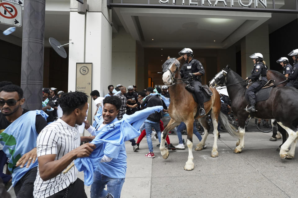 Toronto police on horses push people back during a protest outside of the Sheraton Hotel in downtown Toronto, on Sunday, Aug. 6 2023. The city of Toronto revoked the permit for an Eritrean cultural festival scheduled to run through the August long weekend after a number of violent clashes between participants and protesters sent nine people to hospital and stalled local traffic for hours. (Arlyn McAdorey/The Canadian Press via AP)