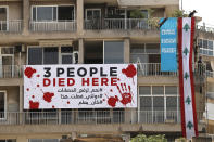 A man, right, hangs a giant Lebanese flag on a building that was damaged during last year's seaport blast during a commemoration in Beirut, Lebanon, Wednesday, Aug. 4, 2021. Lebanon is marking one year since the horrific explosion at Beirut port. The grim anniversary Wednesday comes amid an unprecedented economic and financial meltdown and a political stalemate that has kept the country without a functioning government for a full year. (AP Photo/Hussein Malla)