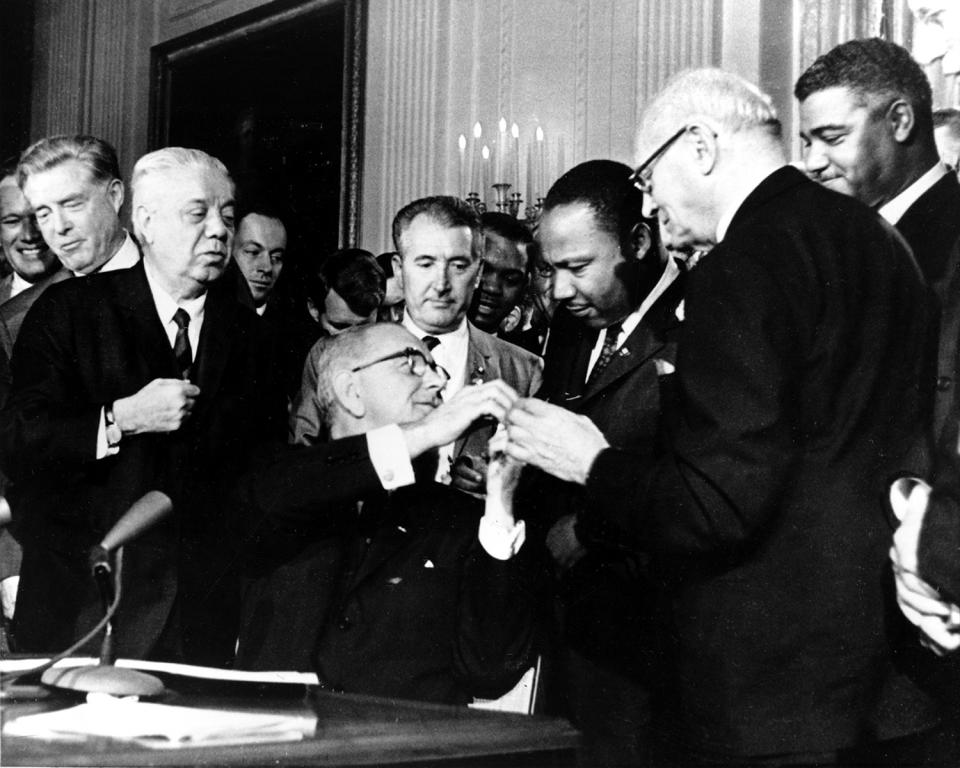 <p>U.S. President Lyndon B. Johnson reaches to shake hands with Dr. Martin Luther King Jr. after presenting the civil rights leader with one of the 72 pens used to sign the Civil Rights Act of 1964 in Washington, D.C., on July 2, 1964. Surrounding the president, from left, are, Rep. Roland Libonati, D-Ill., Rep. Peter Rodino, D-N.J., Rev. King, Emanuel Celler, D-N.Y., and behind Celler is Whitney Young, executive director of the National Urban League. (AP Photo) </p>